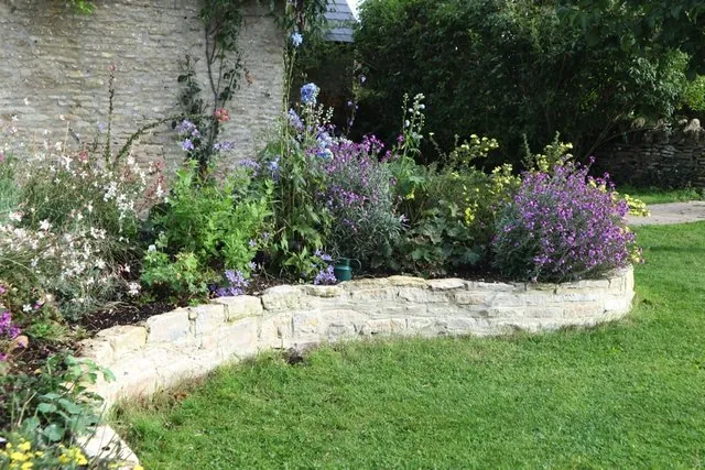 A curved stone-edged border with purple flowers on the lawn